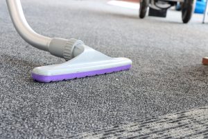 Close-up of a vacuum cleaner attachment on a carpeted floor, focusing on the nozzle and carpet texture.